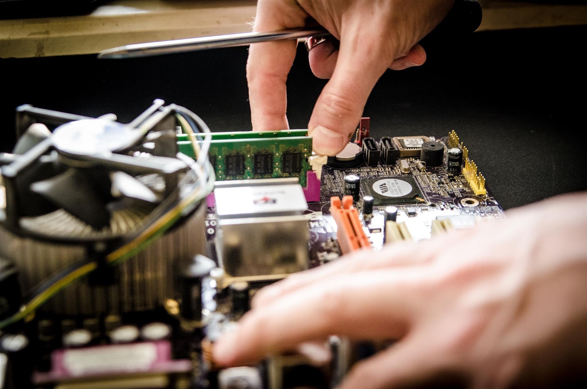 Eine Hand, die versucht von einem Mainboard einen RAM-Riegel zu entfernen